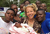 NICHD Director Dr. Diana Bianchi, center holding a baby, surrounded by young people in Kenya.