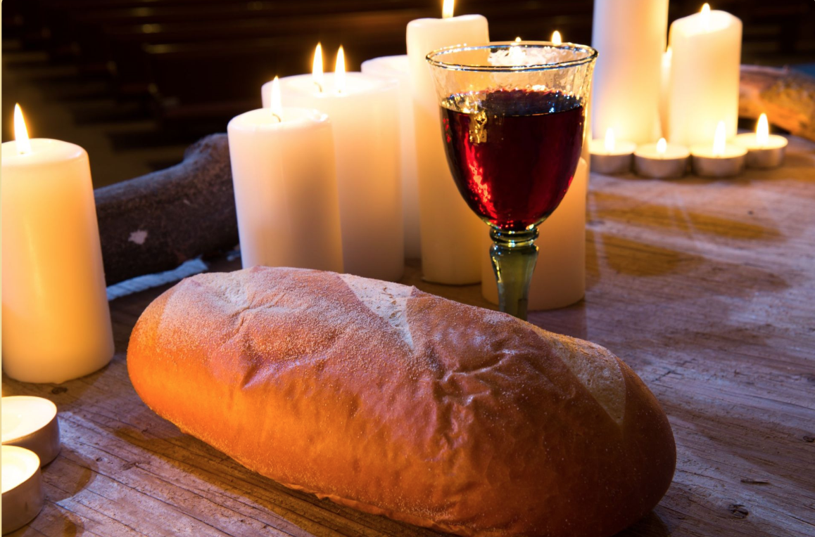 Bread and grape juice on a table with candles in the back 