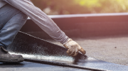 A roofer crouches to lay a strip of tar paper on a flat roof.  