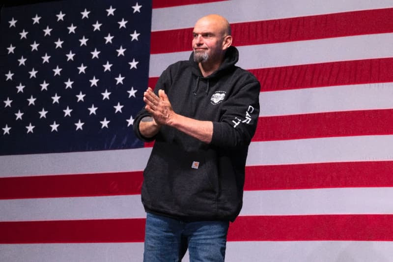 John Fetterman onstage with a large American fla as the backdrop.