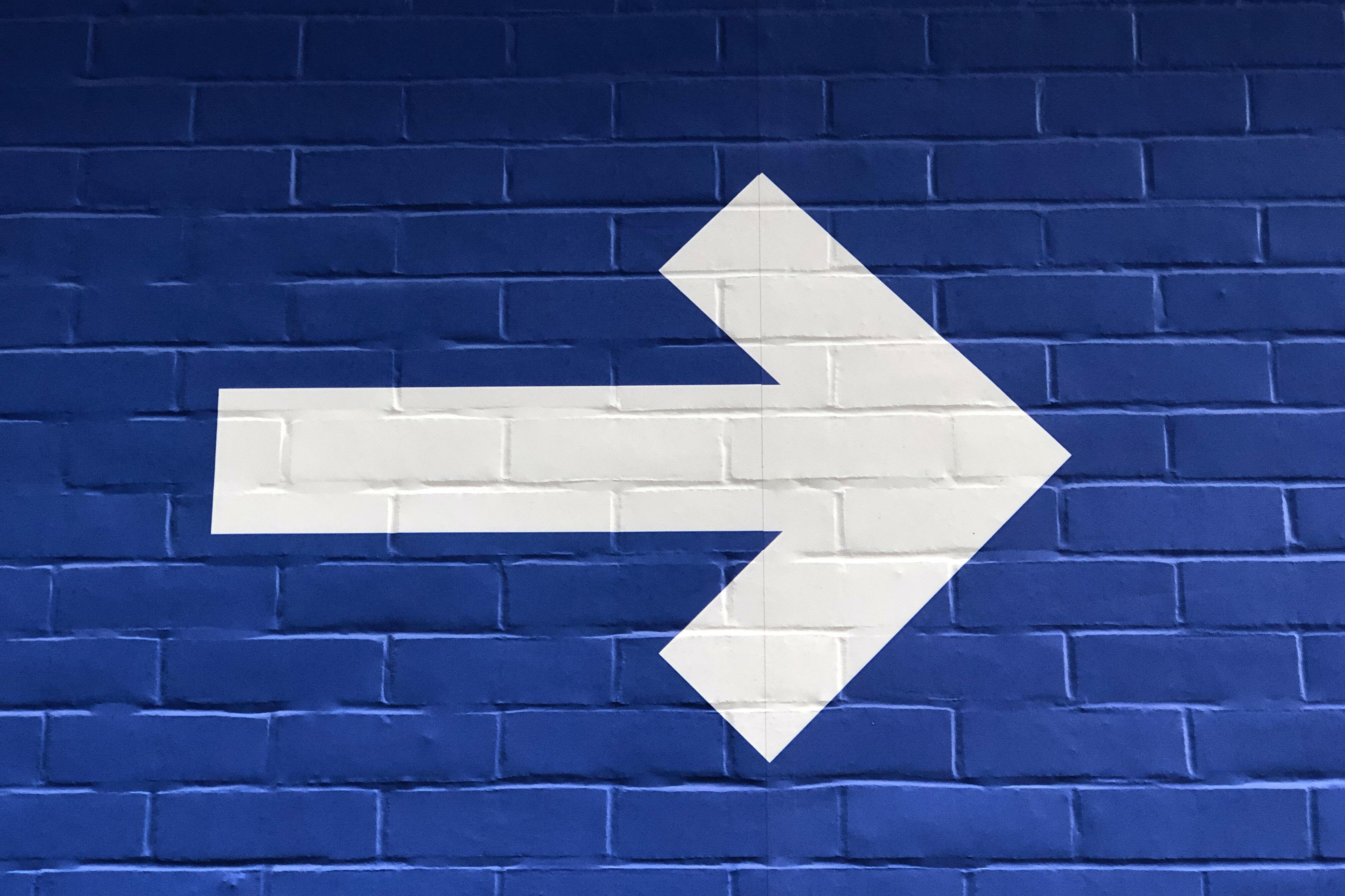 Image of a white arrow on a blue brick background.