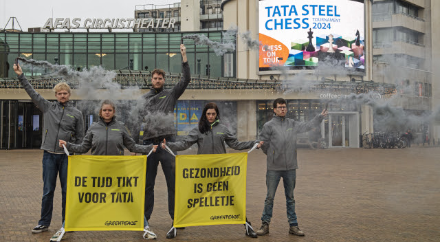 Actievoerders van Greenpeace tonen tijdens het Tata Steel schaaktoernooi hoe dubbel het is dat Tata Steel sponsor is van grote toernooien terwijl het omwonenden van de fabriek ziek maakt.