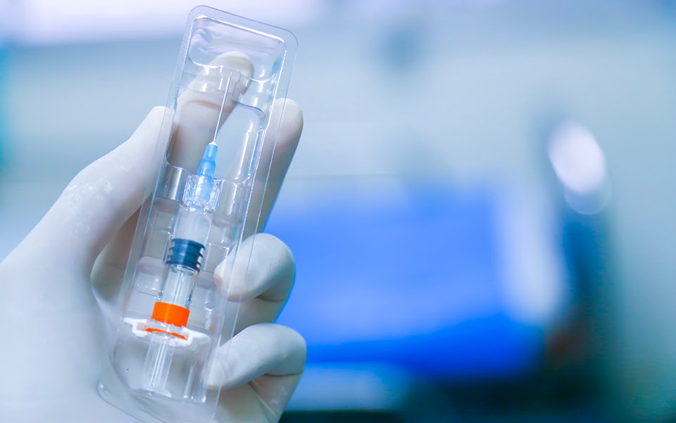 A gloved hand holds a syringe in a plastic case.