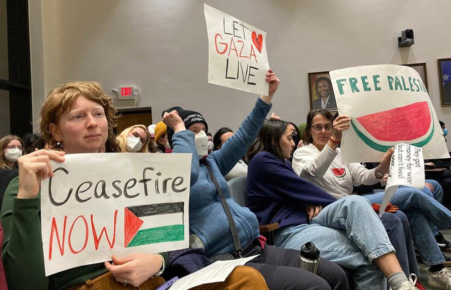 Protesters attending a Durham City Council meeting hold up signs that support a ceasefire in the Israel-Hamas war.