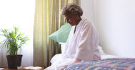 Elderly woman sitting on the edge of her bed.