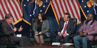 Secretary Walsh addresses three people on a panel in front of U.S. and Labor Department flags.