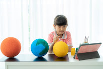 Asian elementary schoolgirl painting the moon in science class learning about the solar system via video conference with teacher and other classmates at home, Homeschooling and distance learning.