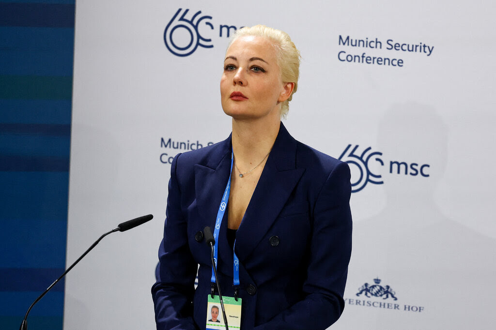 Yulia Navalnaya, in a navy suit, stands at a microphone in front of a backdrop that says "Munich Security Conference."
