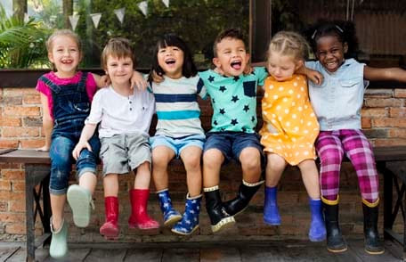 Una fila de niños de varias culturas sonríen y se abrazan. 
