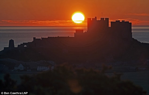 Dawn of summer: The sun rises over Bamburgh Castle in Northumberland at the start of what forecasters are predicting will be a warm week