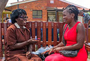 Two women sit on a park bench outdoors, facing each other and speaking together