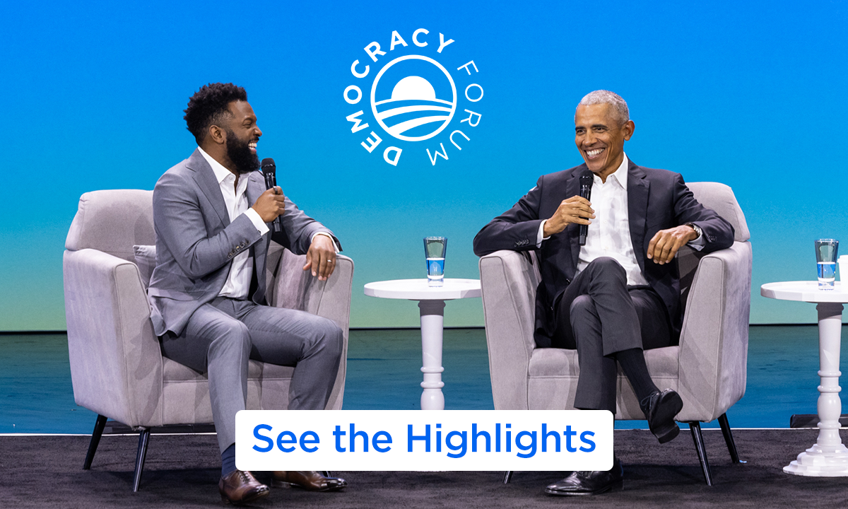President Obama is sitting in a chair and holding a microphone on the right, while on the left, two people with light skintone, one with long hair and one with short hair, sit in matching chairs and look over at him smiling. On the bottom, the words "Sign Up".