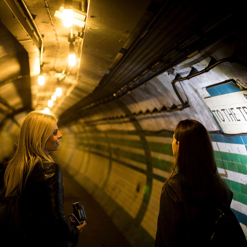 Two women talking in a tiled tunnel at Piccadilly Circus