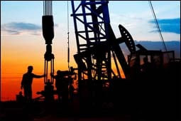 The figure above is a photograph showing oil workers at a derrick at dusk.