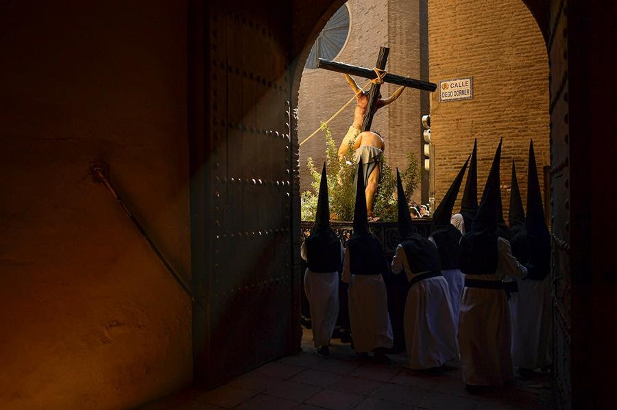 Penitents from the "Exaltacion de La Santa Cruz" brotherhood take part in a Holy Week procession. They are gathered before a depiction of Christ's crucifixion.