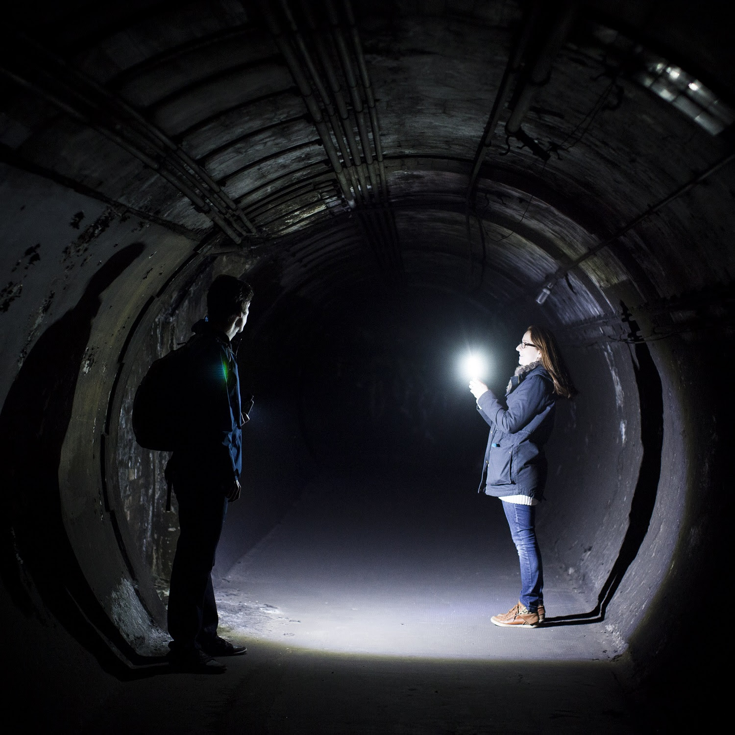 Two people shining a torch into a dark circular tunnel