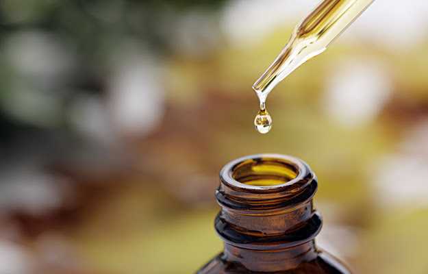 Essential oil dripping into a bottle from an eye dropper.