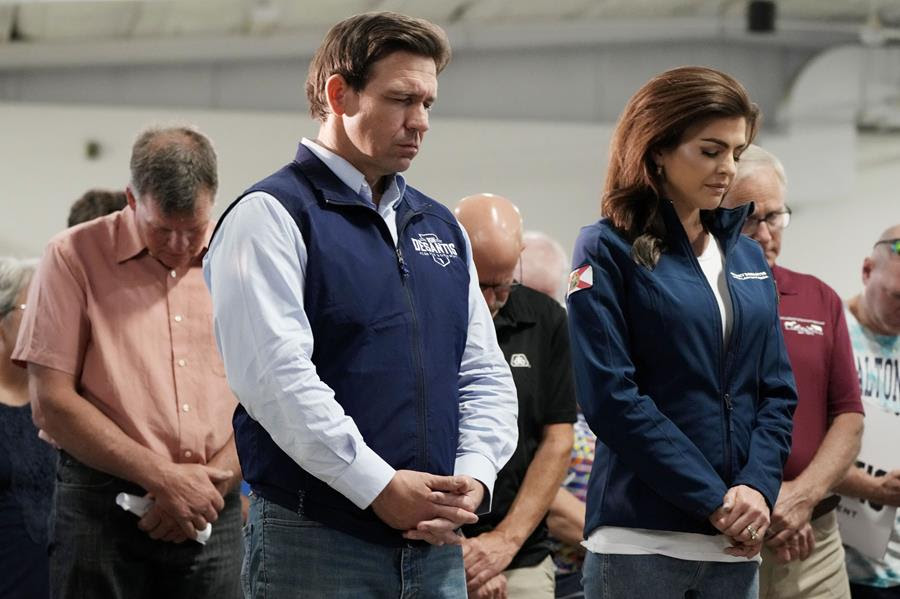 Ron DeSantis and his wife, Casey, pray with their heads bowed at a campaign event.