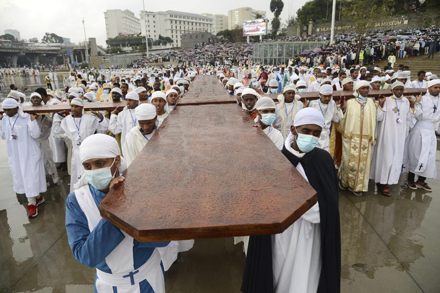 People celebrate the festival of Maskel in Ethiopia on Sunday, Sept. 26, 2021, to commemorate the unearthing of the True Holy Cross of Christ. A massive wooden cross is carried by many people walking together. There are large crowds observing in the background.