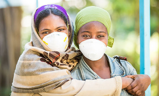 Two women with surgical masks have their arms around each other.