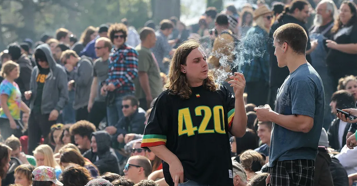 Photo of a crowd of people celebrating 420 in a field. Lots of smoke.