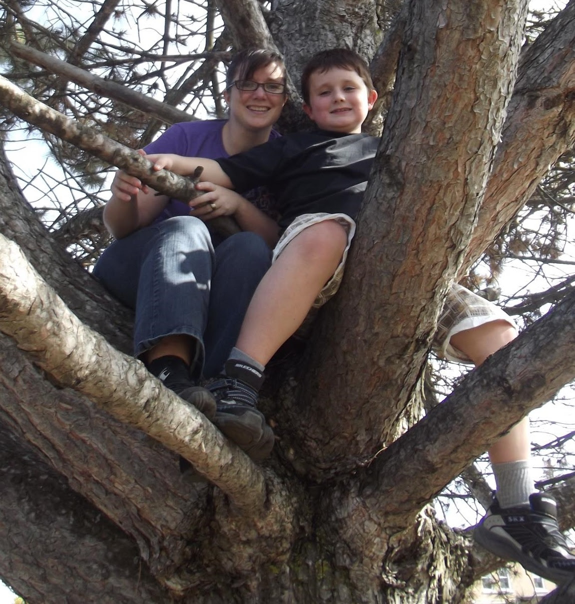 Photo of a smiling mother and child climbing a tree.