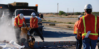 Men in safety gear perform roadwork on a hot day. 