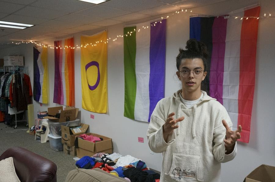 Sean Fisher, one of the student coordinators for QPLUS, the LGBTQ student organization for the College of Saint Benedict and Saint John's University, stands in the organization's dedicated lounge on the college's campus in St. Joseph, Minnesota. There are five different pride flags in the background.