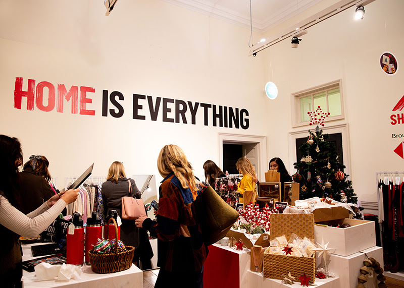 The Shelter Boutique at Somerset House.People are browsing items, and on the wall are printed the words HOME IS EVERYTHING