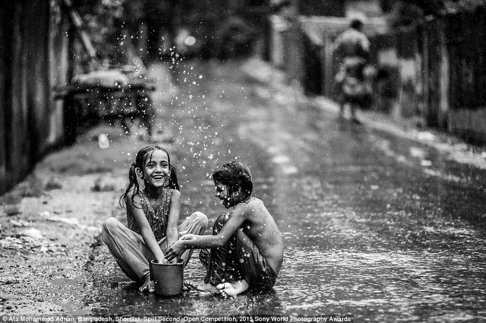 Joy amid hardship: Ata Mohammad Adnan, of Bangladesh, said his photo shows 'two of my young neighbours from the slum nearby enjoying themselves in the rain.' His image is entered into the Split Second category