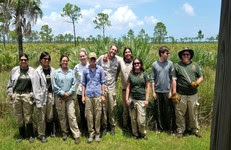 10 FLCC members and volunteers pose in front of scrub land at Savannas Preserve State Park. 