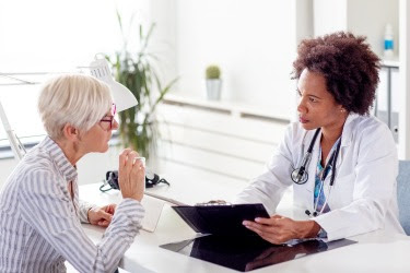The figure is a photo of an older person speaking with a health care provider in an office.