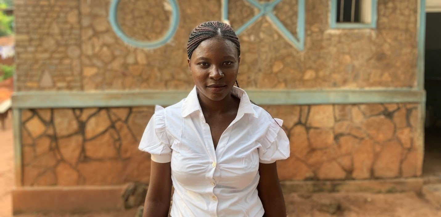 A young woman in a white shirt stands in front of a stone building