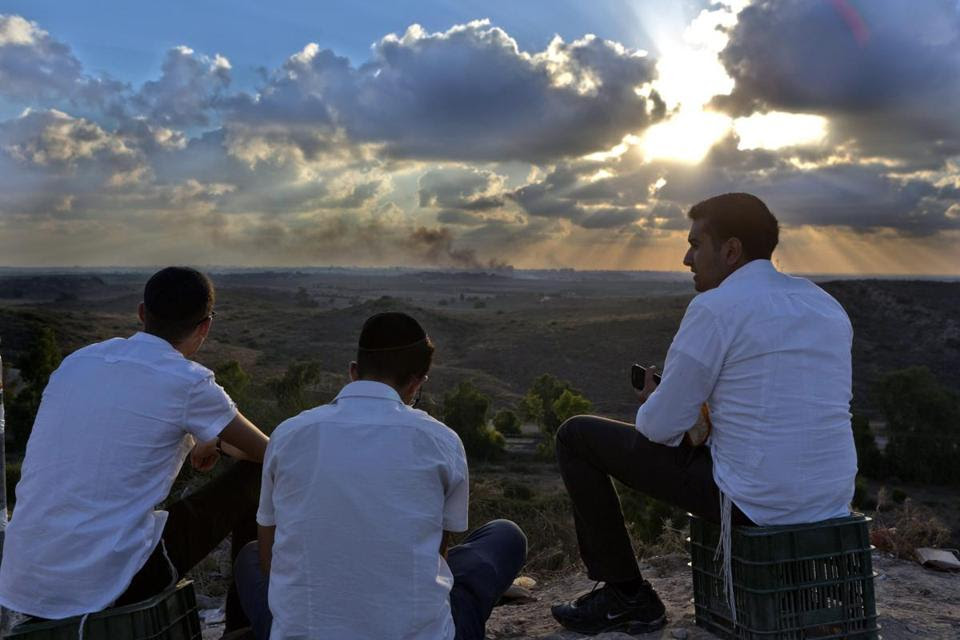 Israelis sat on a hill overlooking the Gaza Strip as smoke rose from the scene of an airstrike.