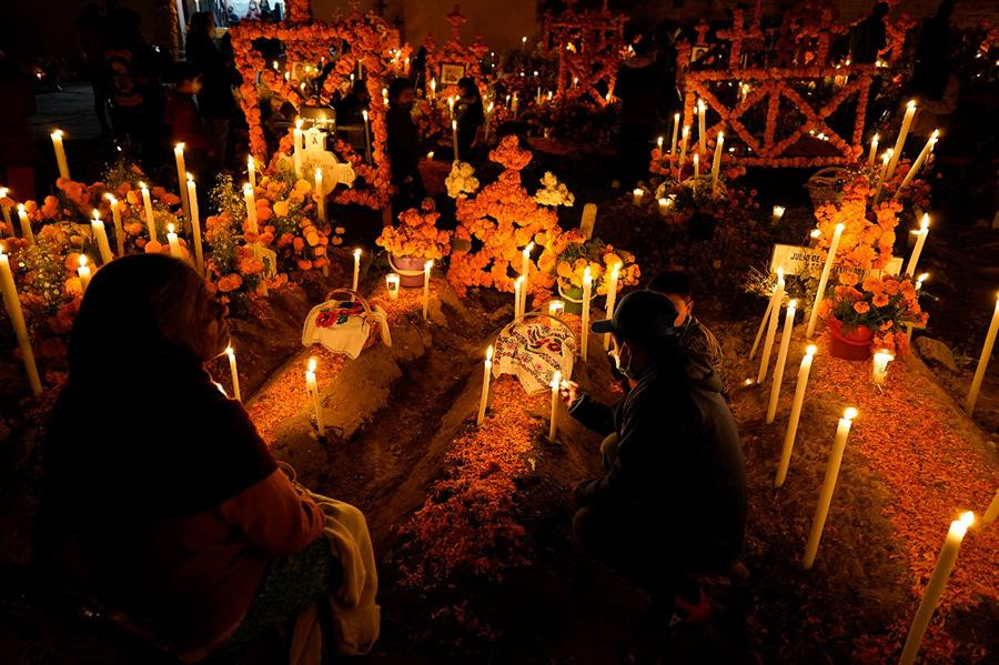 Relatives spend the night next to the tombs of their loved ones during Day of the Dead commemorations at the the Arocutin cemetery in Michoacan state, Mexico, Monday, Nov. 1, 2021. In a tradition that coincides with All Saints Day and All Souls Day, families decorate the graves of departed relatives with flowers and candles, and spend the night in the cemetery, eating and drinking as they keep company with their deceased loved ones. (AP Photo/Eduardo Verdugo)