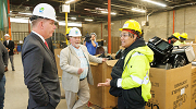 Secretary Walsh chats with two workers in a factory. All are wearing hard hats. 