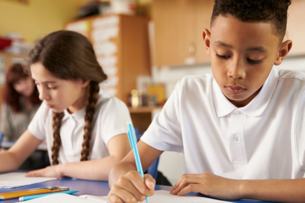 a young girl and a boy in school writing on paper at their desks