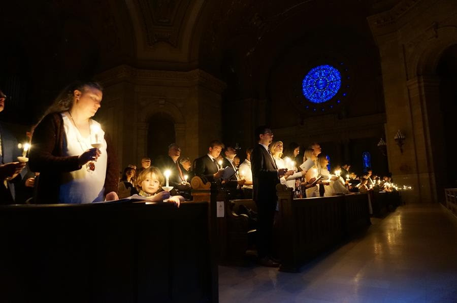 People holding lit candles stand in the pews of a church.