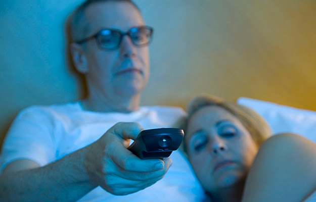 A sleepy couple watching TV in bed.