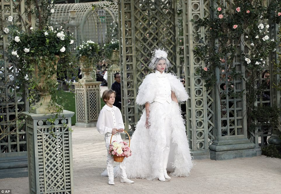 Todo branco: um modelo usa uma criação para a coleção de moda Chanel Haute Couture Spring-Summer 2018 ao lado de um menino de flores 