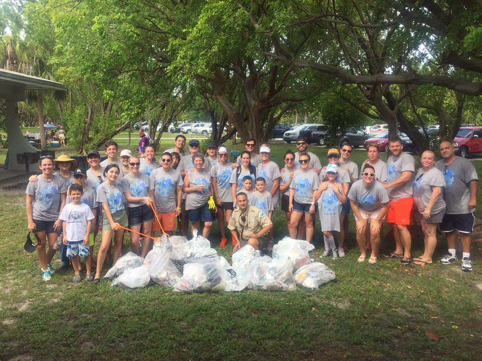 Group of Norwegian Cruise Line employees and park ranger stand behind bags of trash collected during event.