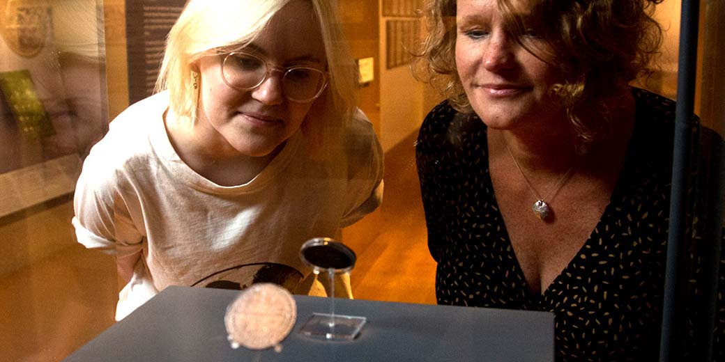 Two people look through a glass case at a coin on display