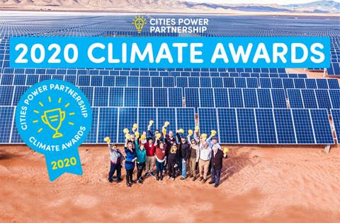 Aerial photo of a group of people standing in front of solar panels with their arms in the air.