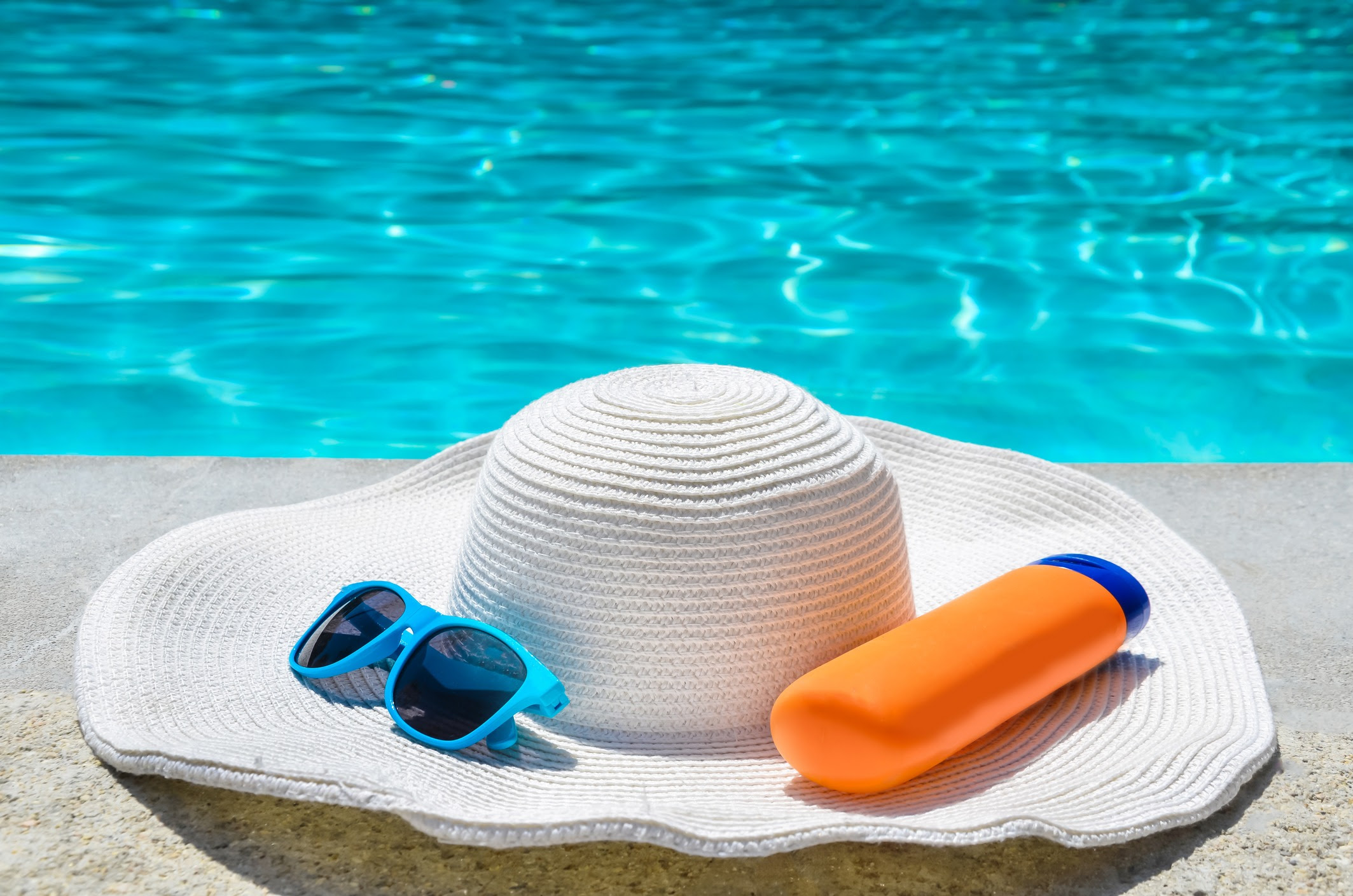 Hat, sunscreen, and sunglasses near a pool