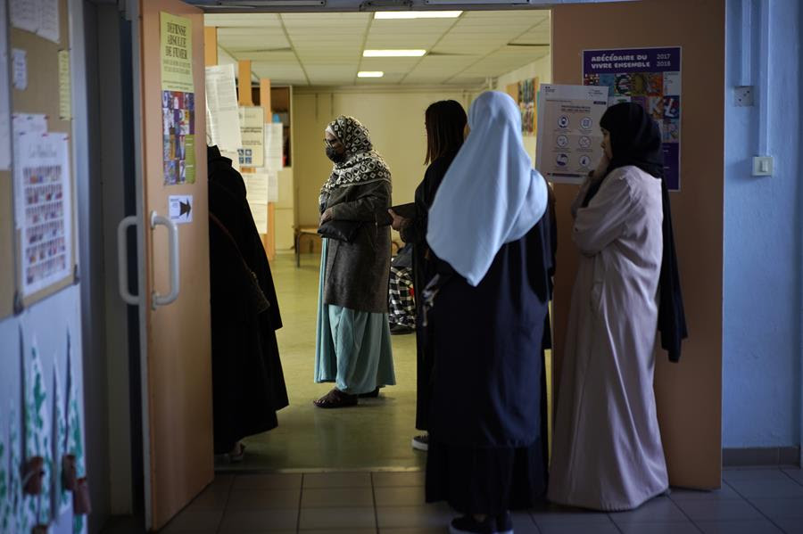 Women wearing long robes wait in line to vote.