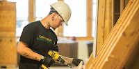 A young man in a hardhat and protective glasses uses a drill on a construction site.  