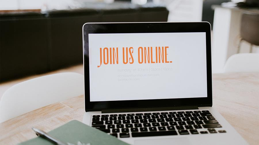 A laptop screen with orange text that says "Join us online." In the foreground is a notebook with a pen clipped to it.
