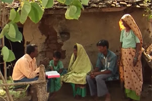 A man is sitting with his Bible open. He is speaking to a group of people.