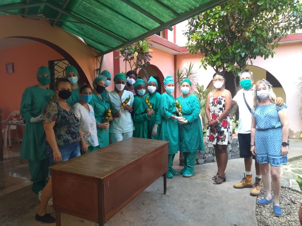 Photo of a group of Cuban health workers wearing PPE, standing in a sunny courtyard.