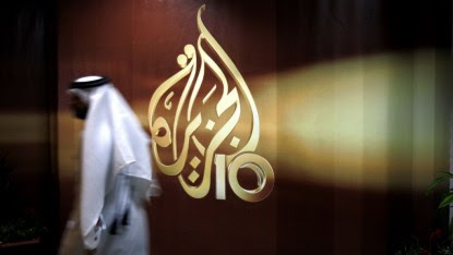 A Qatari employee of al-Jazeera TV walks past the logo of Al Jazeera in Doha, Qatar, November 1, 2006 (AP Photo/Kamran Jebreili, File)